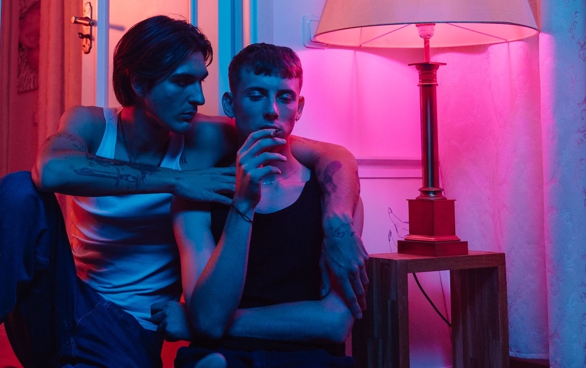 Two young men sitting together in a room lit by a pink lamp